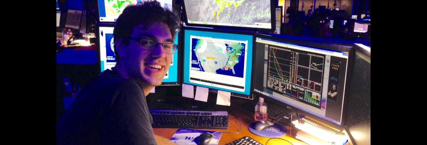 A man sits at a desk in front of a computer that is showing atmospheric graphs.