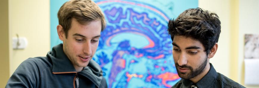 A close up of two men with an image of a brain on the wall behind them.