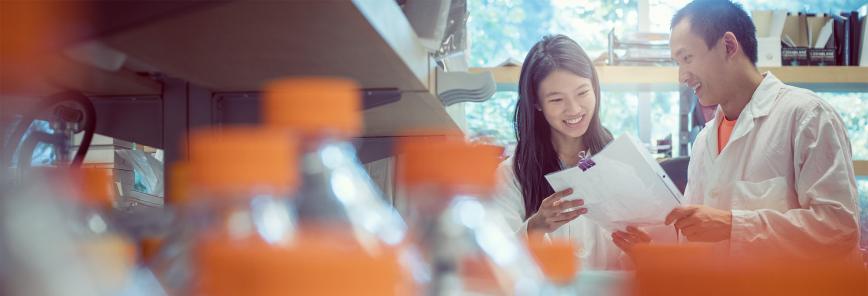 Two people stand in a lab looking together at a lab report. 