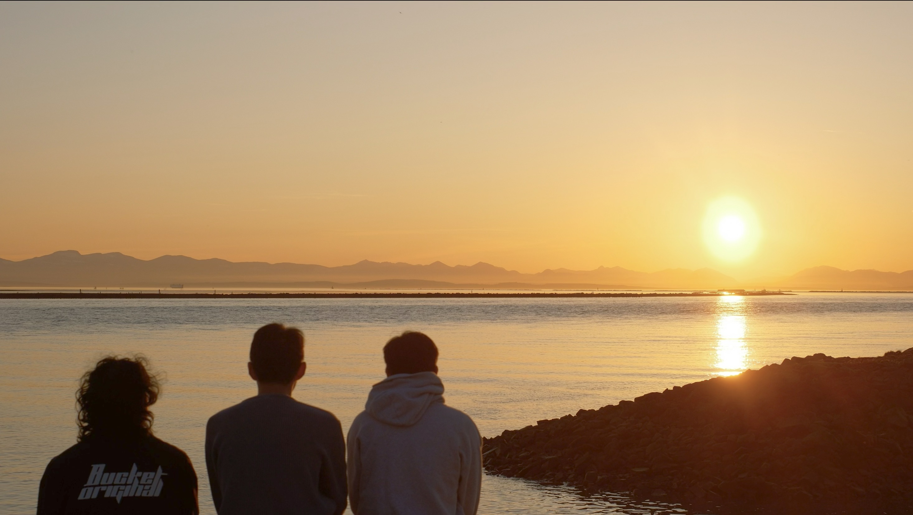 UBC Science Co-op Environmental Sciences student Eric Fang sits with two friends at the beach at sunset.