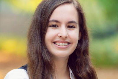 UBC Science Co-op Physics and Astronomy student Madison Levagood smiles in front of a blurred forest background.