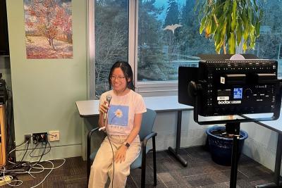 UBC Science Co-op Cognitive Systems (Computational Intelligence and Design) student Rachel Chiu sits in a chair and speaks into a microphone.