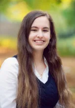 UBC Science Co-op Physics and Astronomy student Madison Levagood smiles in front of a blurred forest background.