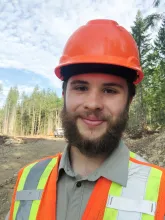 UBC Science Co-op Environmental Sciences student Markus Hanson smiles in a hardhat in front of a forest.