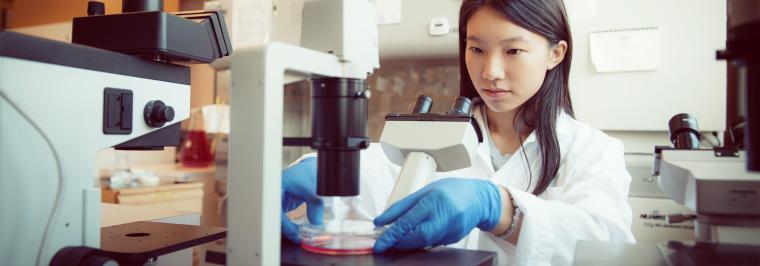 A woman looks at a microscope.