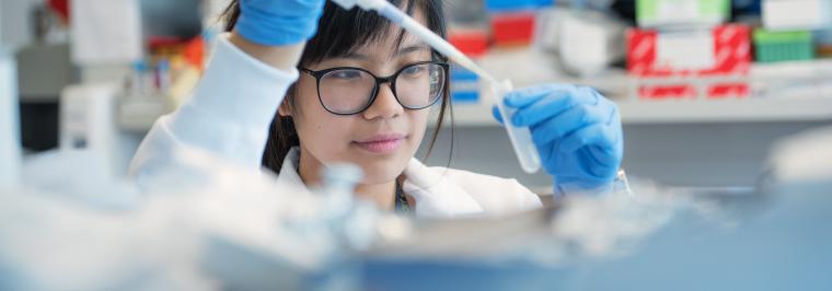 A woman uses a pipette in a lab.