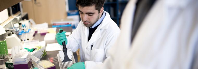 A man pipettes at a lab table.