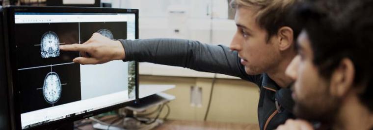 Two men look at a computer screen together.