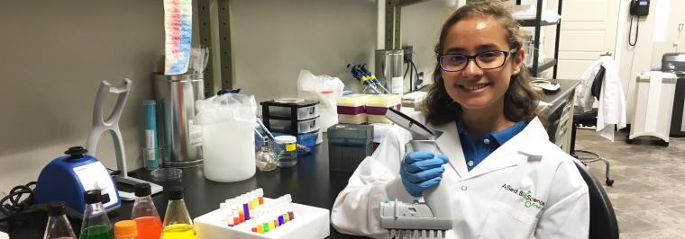 A woman sits at a lab table.